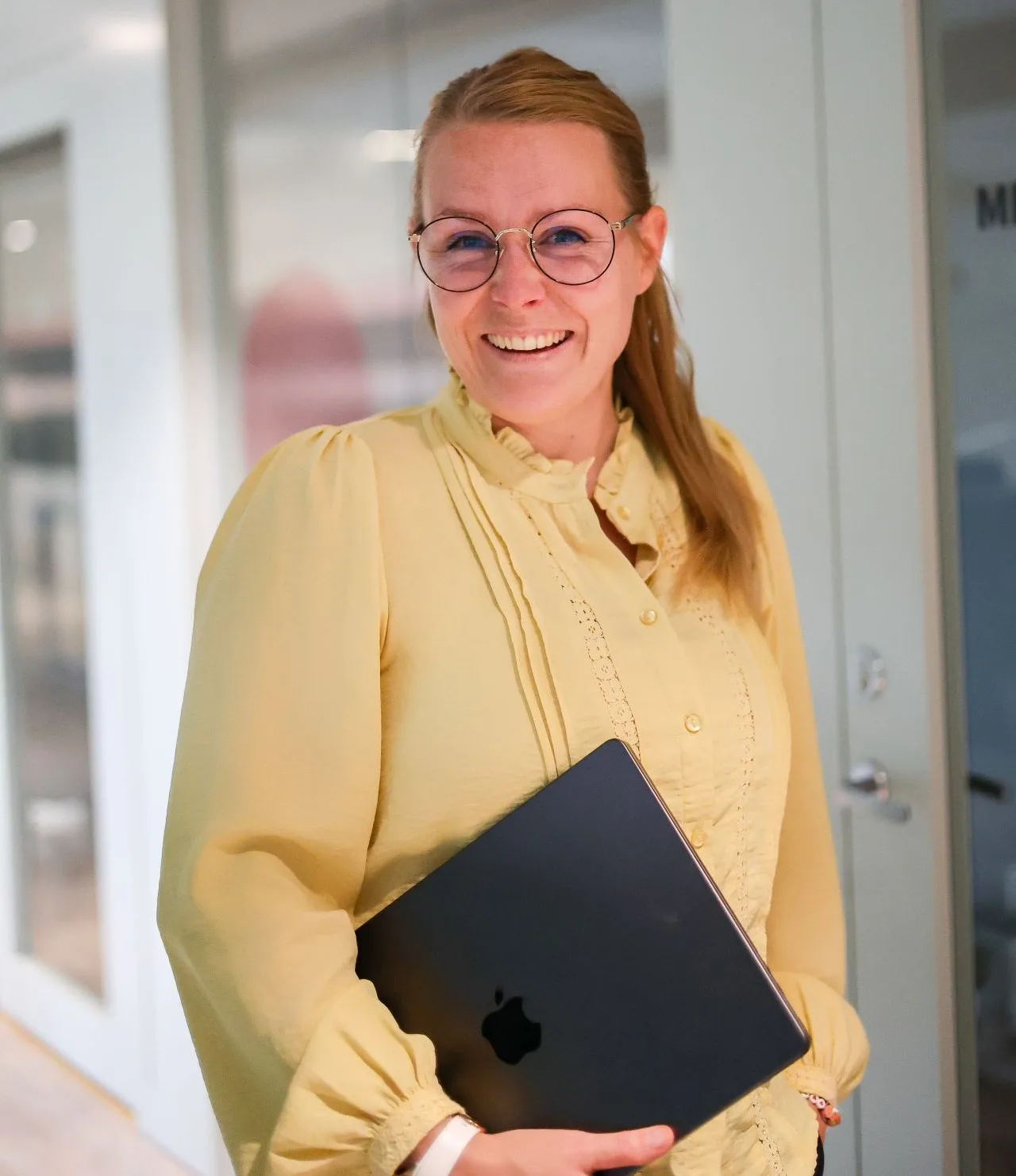 Tina Algeskär i gul blus med en bärbar dator i händerna